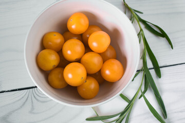 Yellow cherry tomatoes in a bowl on the wooden white table. 