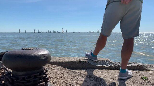 Man&rsquo;s legs and yacht silhouettes on the horizon. A man watching regatta in Nida, Lithuania.
