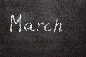 Fototapeta premium Month written in white chalk on a chalkboard. The month depicted on the chalkboard is March