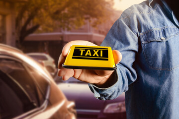 Male hand in jeans shirt holding taxi sign on evening street parking lot.