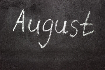 Fototapeta premium Month written in white chalk on a chalkboard. The month depicted on the chalkboard is August