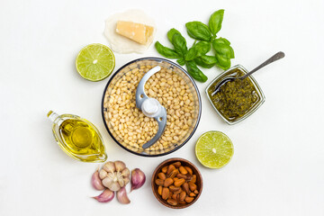 Homemade pesto sauce and ingredients. Cutter with pine nut, unpeeled pine nuts in bowl, olive oil, pesto bowl, basil leaves, parmesan, garlic, lemon.