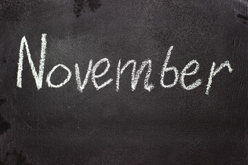 Fototapeta premium Month written in white chalk on a chalkboard. The month depicted on the chalkboard is November