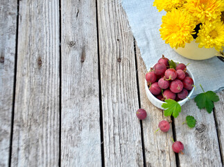 yellow flowers in a cup next to a cup with gooseberries on a wooden rustic background with selective focus