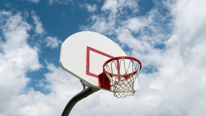 Blue, partly cloudy skies behind a lone basketball hoop.