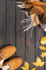 Autumn Fashion Concept. Brown Orange leather women boots with fur, checkered warm plaid, golden autumn leaf on brown wooden background top view. Fashionable women's footwear. Cozy fall composition