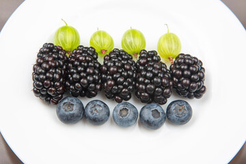 berries blueberries, gooseberries and blackberries on a white plate. useful vitamin healthy food fruit. healthy vegetable breakfast