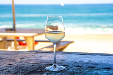A glass of white wine on wooden table of outdoor restaurant on the beach. Sea view. Summer beach vacation. 