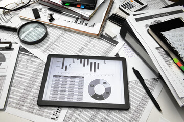 business office desk closeup - tablet computer with tables and graphs on the screen, financial reports, analysis and accounting, set of documents for bookkeeping