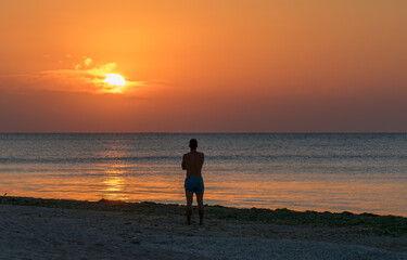 The man sits alone on the beach and admires the sunrise. Meditation, relaxation