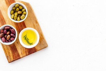 Olives and olive oil in bowls on cutting board on white top view copy space
