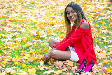 Beautiful young African girl collects autumn leaves in the Park