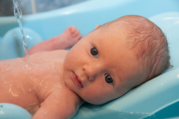 Newborn baby in a bath under running water