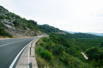 Mountain serpentine road with a fence near the cliff and views of the green hills and mountains.