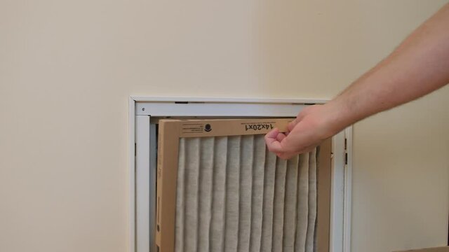 HVAC service technician replacing dirty indoor air filter in residential heating and air conditioning system. Home air duct ventilation system maintenance for clean air.