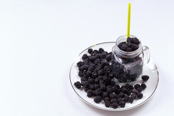 Black and blue ripe blackberries, in a glass Cup on a plate on a white background. Healthy dessert. Space for text. Mockup