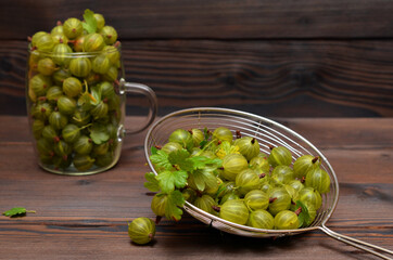 gooseberry berries in a colander and glass mug on a dark background close-up