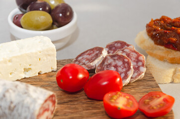 Salami chorizo and slice of goat cheese served on wooden board with olives and bread toast, traditional Spanish tapas 