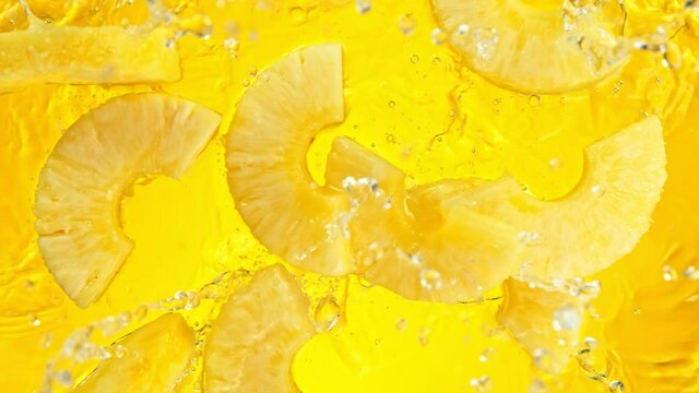 Super Slow Motion Shot of Pineapple Slices Falling into Water on Yellow Background at 1000fps.
