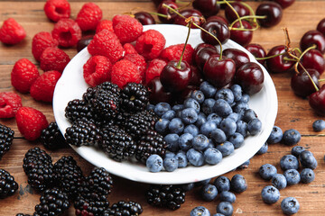 Raspberries, cherries, blackberries, blueberries. View from above. Fresh organic berries in a round plate on a wooden table background.