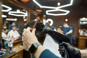 Close up view of a barber or hairdresser drying the hair of a young guy visiting modern barber shop