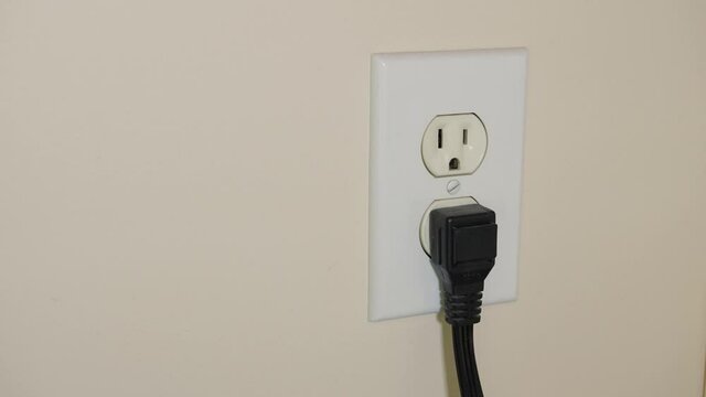 Close up of male hand unplugging electrical power cord from residential wall electricity outlet.