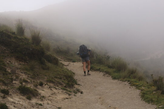 A backpacker hiking through misty mountains while struggling with her heavy backpack