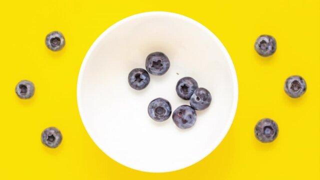 Close up blueberry disappear from white bowl on yellow background from adobe. Stop motion animation. Food and vegetarian concept