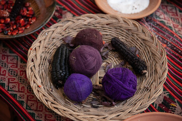 Fototapeta na wymiar Balls of wool that have been colored purple by a natural paint made by the black maiz that is laying next to it