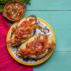 Mexican molletes with bacon and pico de gallo sauce on turquoise background