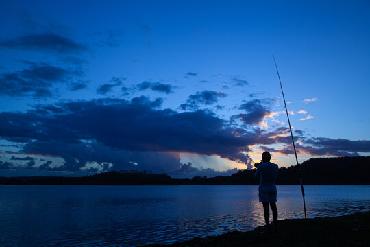silhouette of a man playing trumpet and fishing at lake shore