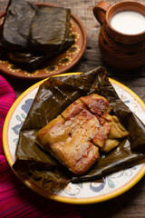 Mexican tamales in banana leaves on wooden background
