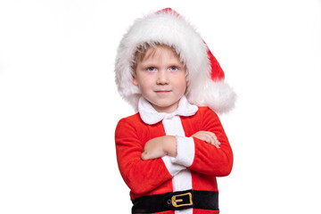 A child boy in a red suit and a santa claus hat stands with his hands on his chest. Positive story about Christmas and New Year 2021, confident and cheeky kid to look at the camera with a challenge.