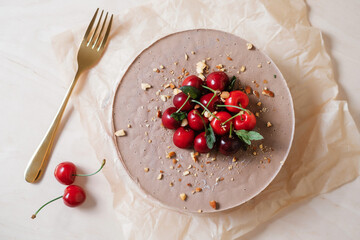 Homemade chocolate cake with cherry on parchment paper. Food delivery. Homemade baking. Top view. Delicious tart with chocolate and cherry on the wooden with golden fork.