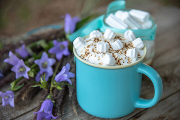 Delicious cappuccino with caramel and marshmallows in a light blue mug. In nature with flowers.