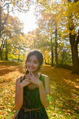 Young happy Asian woman smiling and thinking surrounded by scenic autumn trees in the forest