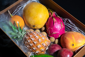 Photo of wooden box with different exotic fruits in smoke