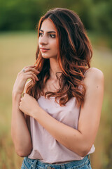 Naklejka premium Portrait of beautiful sexy young woman with long brown hair in pink tank top and denim shorts posing outdoors, sensual, serious