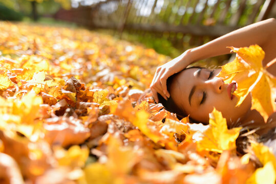 Young beautiful Asian woman lying down with eyes closed on yellow autumn leaves - Powered by Adobe