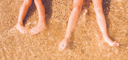 Summer holiday and leisure concept. Top view of children's feet on the sand by the sea. Horizontal image.