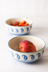Blue bowls with apples and cherries on a white background  in daylight.