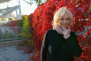 Senior woman holding scarf in front of red creeper plants covering the fence