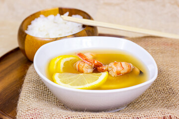 White bowl with traditional light spicy thai cuisine tom yam soup with shrimps, seafood and lemon on wooden board background.