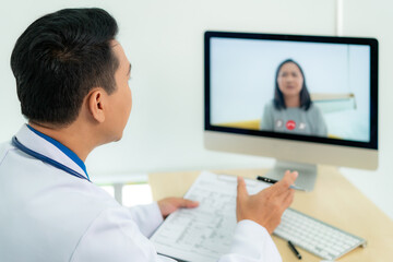Asian man doctor wears white coat and headset speaking videoconferencing on laptop computer using...