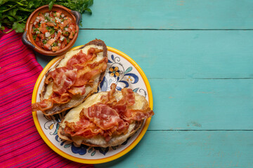 Mexican molletes with bacon and pico de gallo sauce on turquoise background