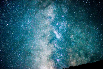 The core of the Milky Way galaxy lights up the night sky and is seen over a partial rocky ridge line.