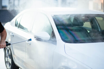 Summer car wash. Cleaning the car using high pressure water. Car wash with soap. Close up concept. Close up photo of a man hands washes his car Concept disinfection and antiseptic cleaning. Car wash.