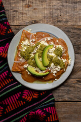 Mexican enfrijoladas with green sauce on wooden background