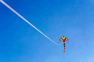 a flying rainbow-colored kite attached to a long string with bright clear blue sky in the background. LGBT people of color. The string is out-of-focus. A kite as a symbol of freedom. Copy space.