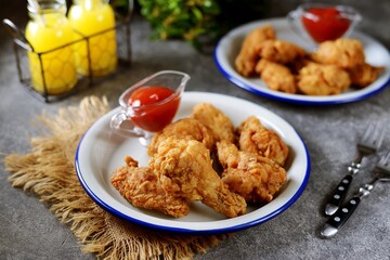 Delicious homemade deep fried breaded chicken wings with tomato sauce on a gray background.